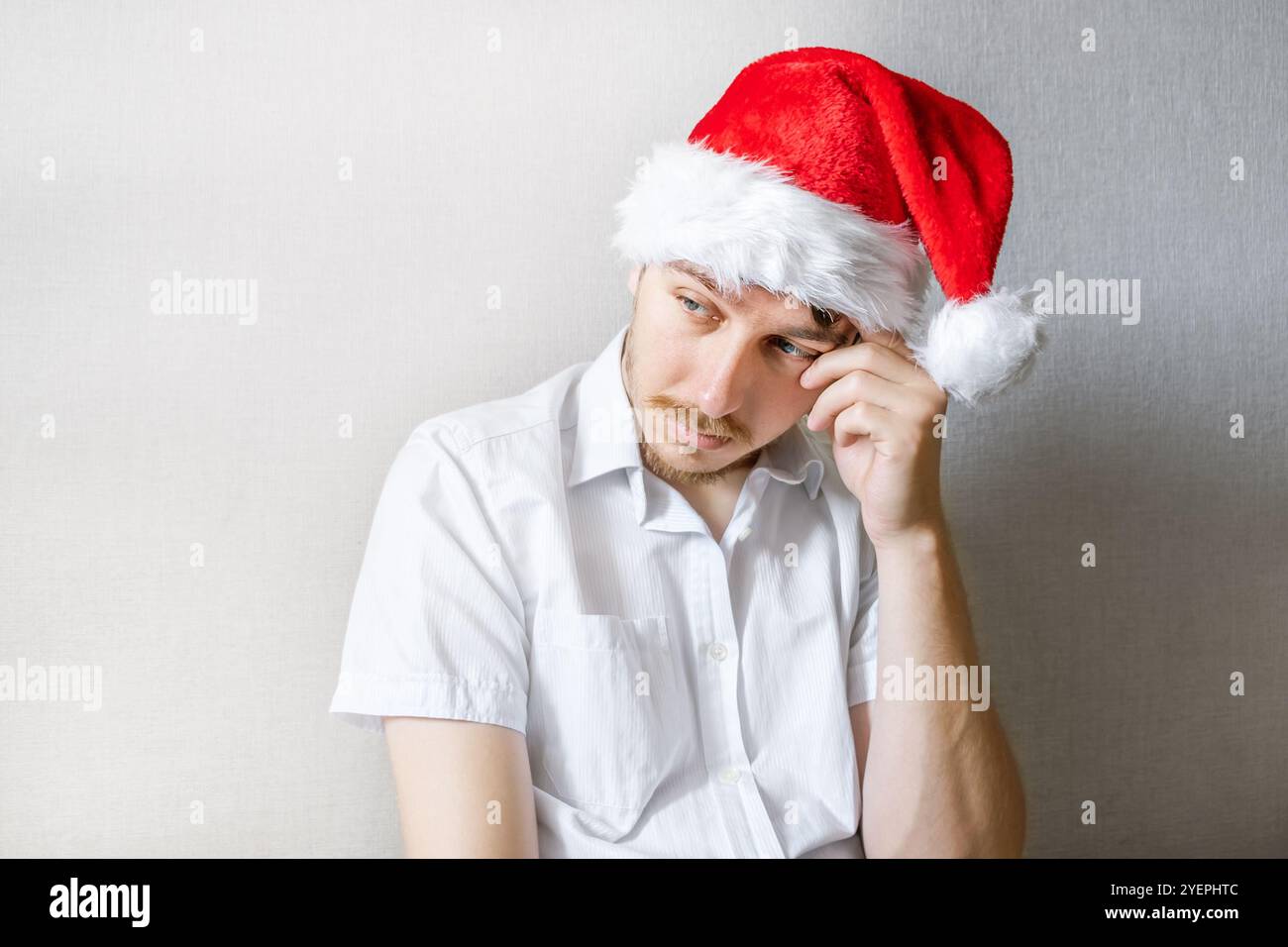 Sad Young Man in Santa Hat by the Wall in La camera Foto Stock