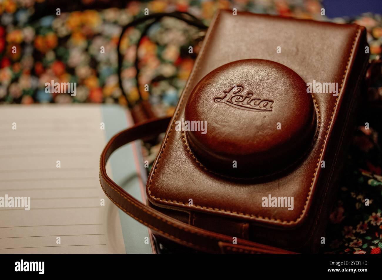 Madrid, Spagna. 1 maggio 2023 fotocamera Leica d'epoca in custodia in pelle marrone appoggiata sul tavolo su sfondo floreale. Sfondo dei viaggi estivi. Fotografia retrò. Foto Stock