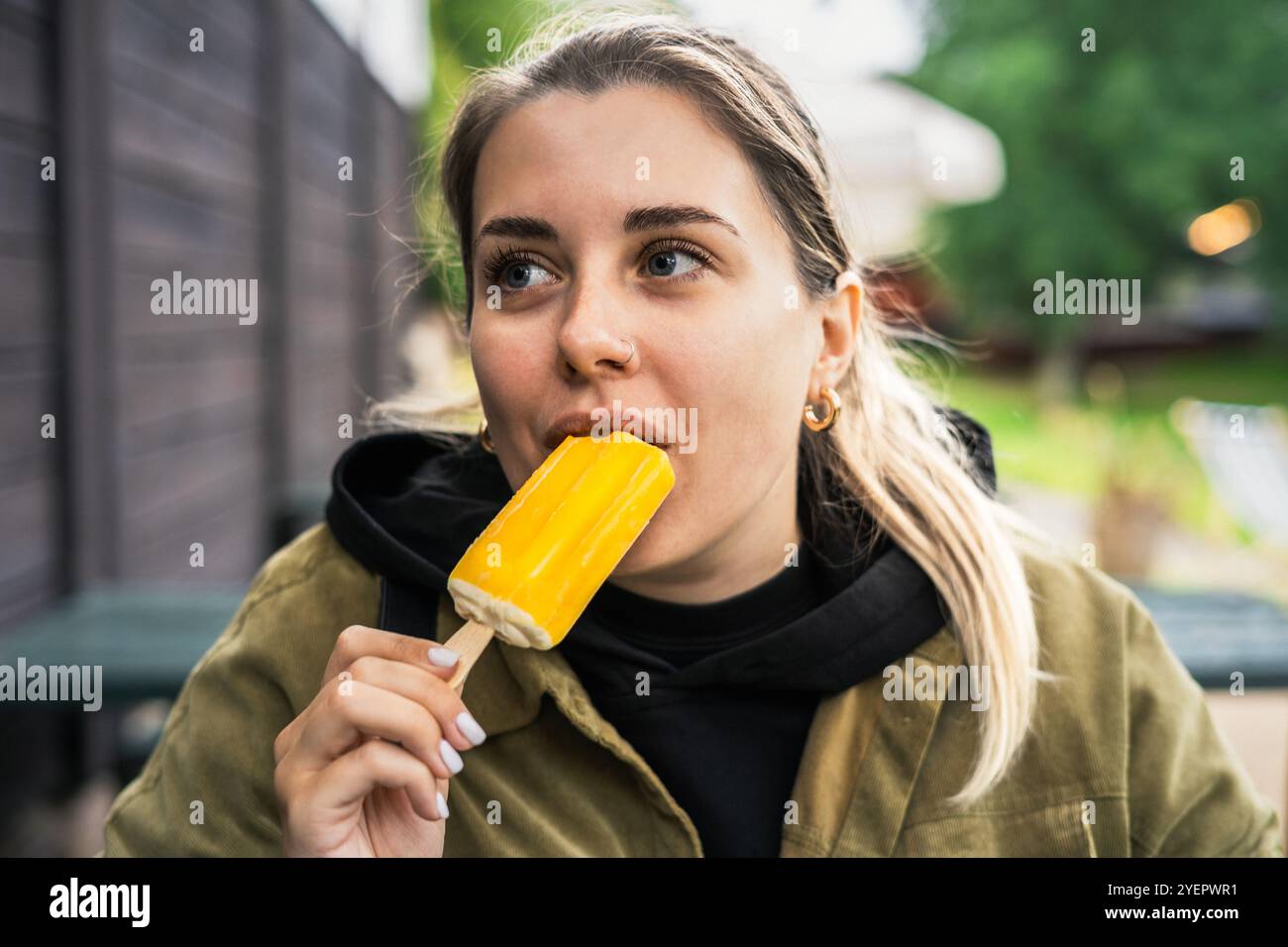 Una giovane donna che mangia un gelato giallo su un bastoncino Foto Stock