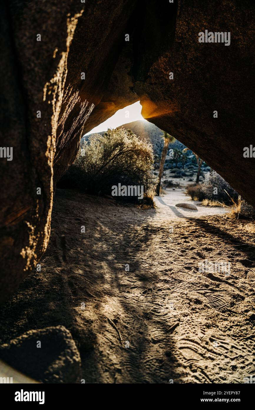 La luce del sole sbircia attraverso le rocce, illuminando il terreno sabbioso Foto Stock