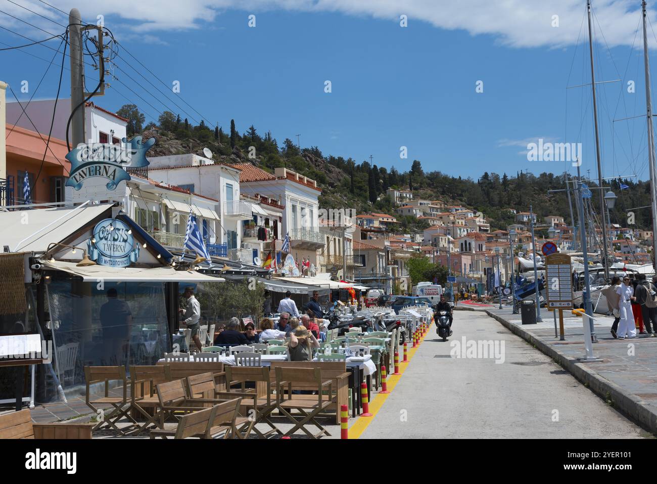 File di ristoranti lungo un porto affollato in una città costiera greca, annidata tra colline soleggiate, passeggiata, Poros, isola di Poros, isole Saroniche, Peloponneso Foto Stock