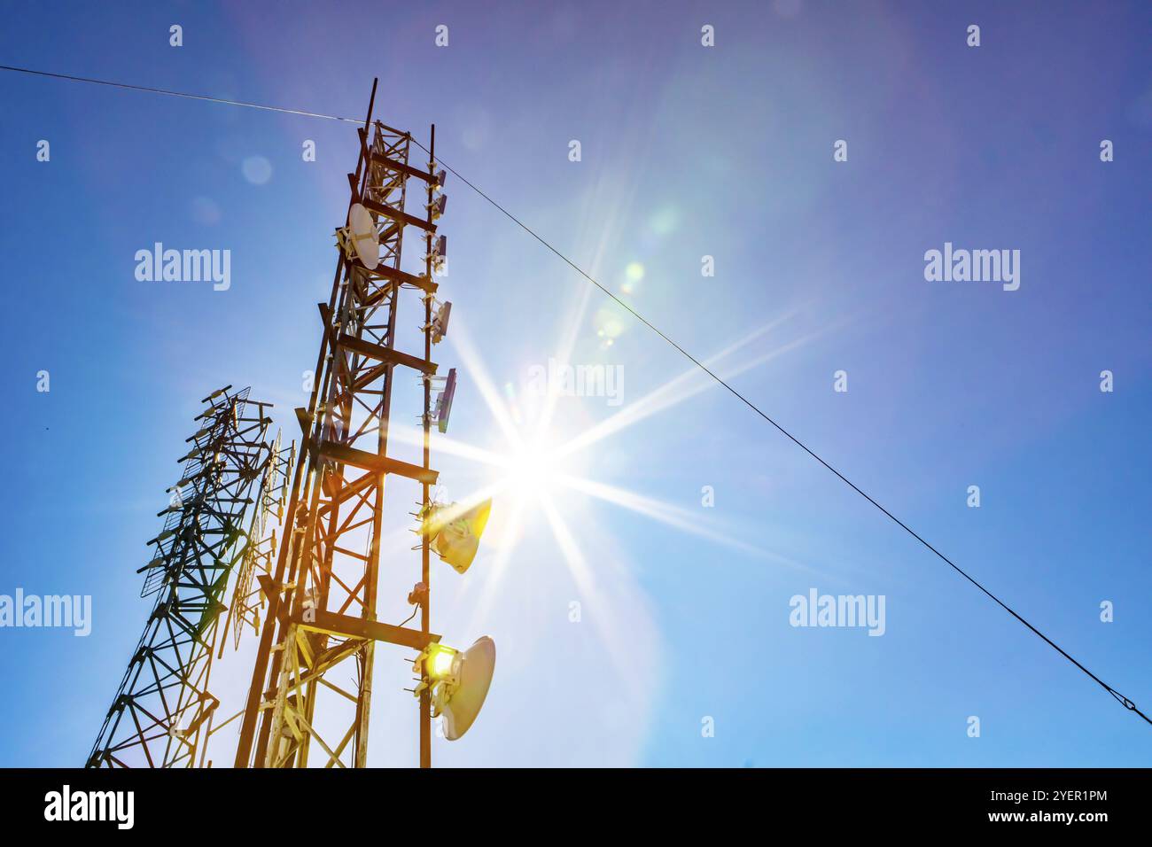 Un basso angolo di visione di due mobili di comunicazione trasmettitore di dati e del segnale GPS torri, contro un cielo blu con sole luminoso brillare e colorate lens flare Foto Stock
