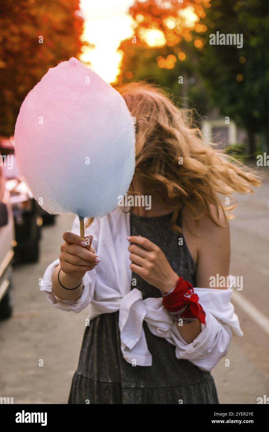 Carino e bella giovane ragazza o studente, mangia e posa con zucchero blu di cotone caramella sulla strada della città, concetto Happy Times. Stile di vita. Giovane ragazza sorridente Foto Stock