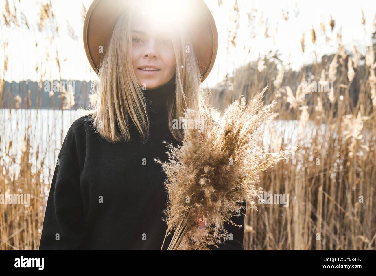 Donna bionda europea con cappello beige in pullover nero in campagna. Ora d'oro, cotagecore. Viaggi locali. Vita lenta. Salute mentale. Messa a terra a. Foto Stock