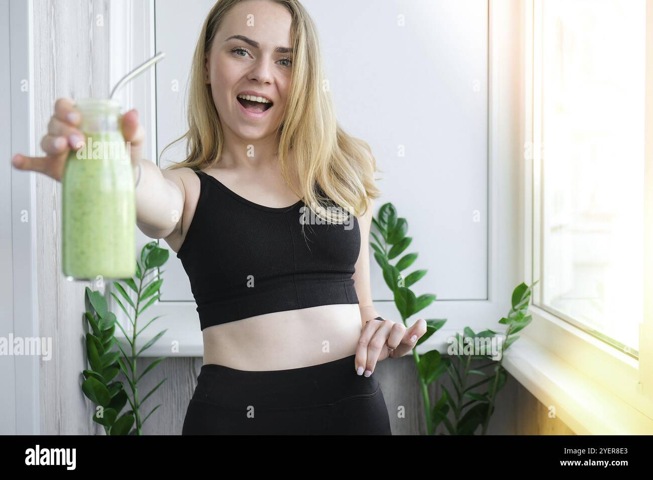 Giovane donna bionda millenaria bevendo frullato vegano bevanda detox. Donna che fa esercizi di yoga a casa. Mangiare pulito, perdita di peso, cibo sano dieta c Foto Stock