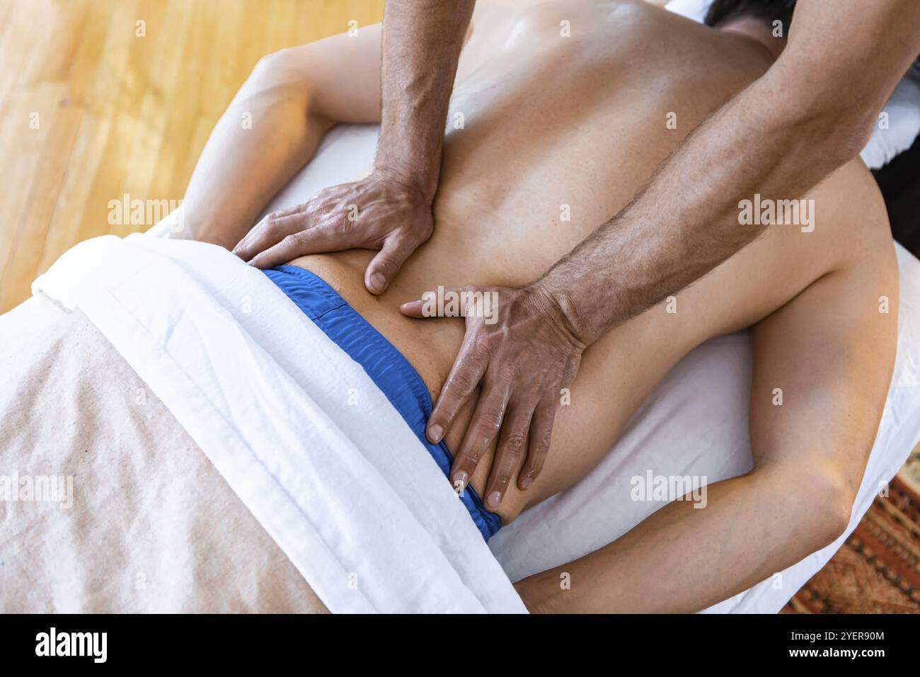 Un maschio irriconoscibile sdraiato sul tavolo e che riceve il massaggio alla schiena da un massaggiatore professionista. Vista dall'alto Foto Stock