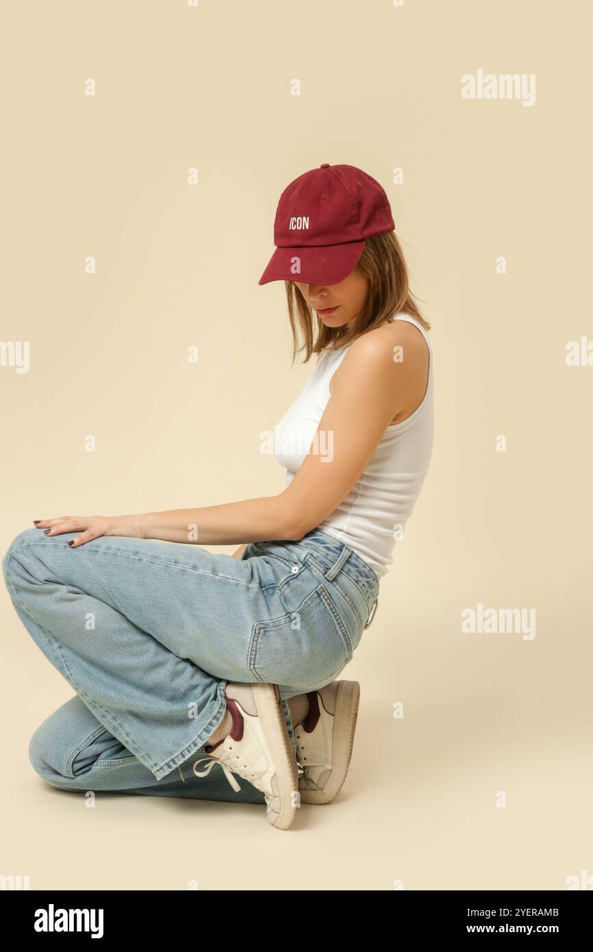 Serie di foto in studio di donna in classico abito base - jeans blu e canotta bianca e cappellino rosso da baseball Foto Stock