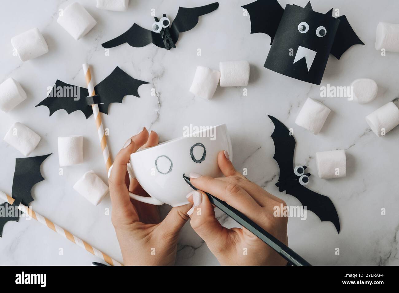 Le mani femminili dipingono sui jack di paura della tazza bianca faccia DIY per i capretti Halloween domestico attività di festa arte bambini mestiere decorazioni fatte a mano. Passo dopo passo Foto Stock