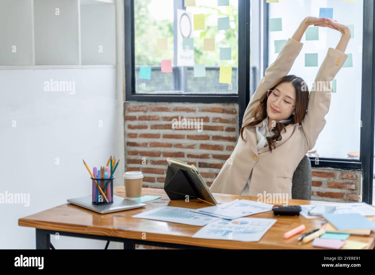 Giovane donna d'affari stanca che si allunga le braccia e la parte superiore del corpo mentre è seduta alla scrivania dell'ufficio Foto Stock