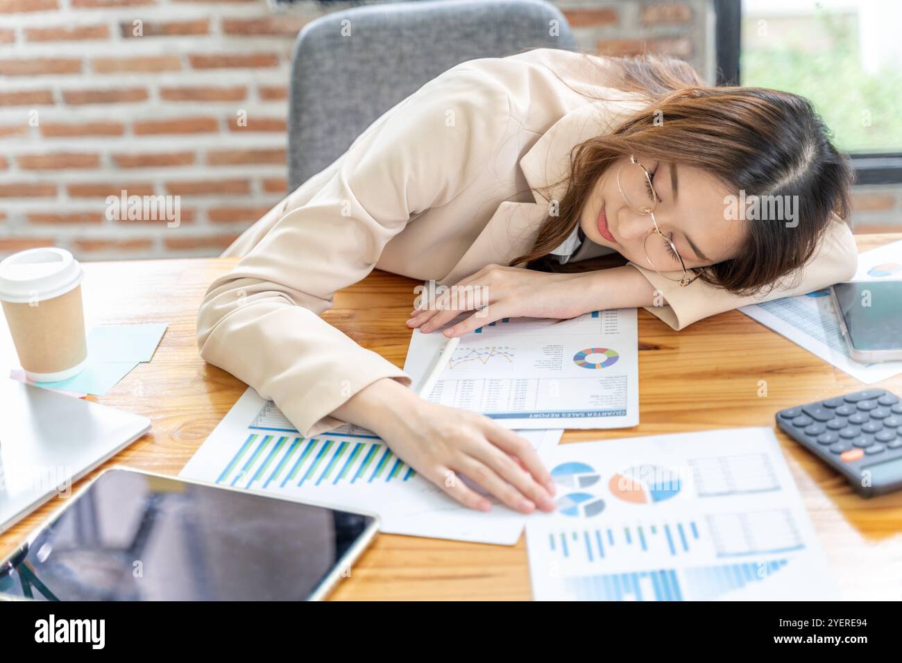 La giovane donna d'affari stanca abbassa la testa sul braccio dormendo alla scrivania del suo ufficio Foto Stock