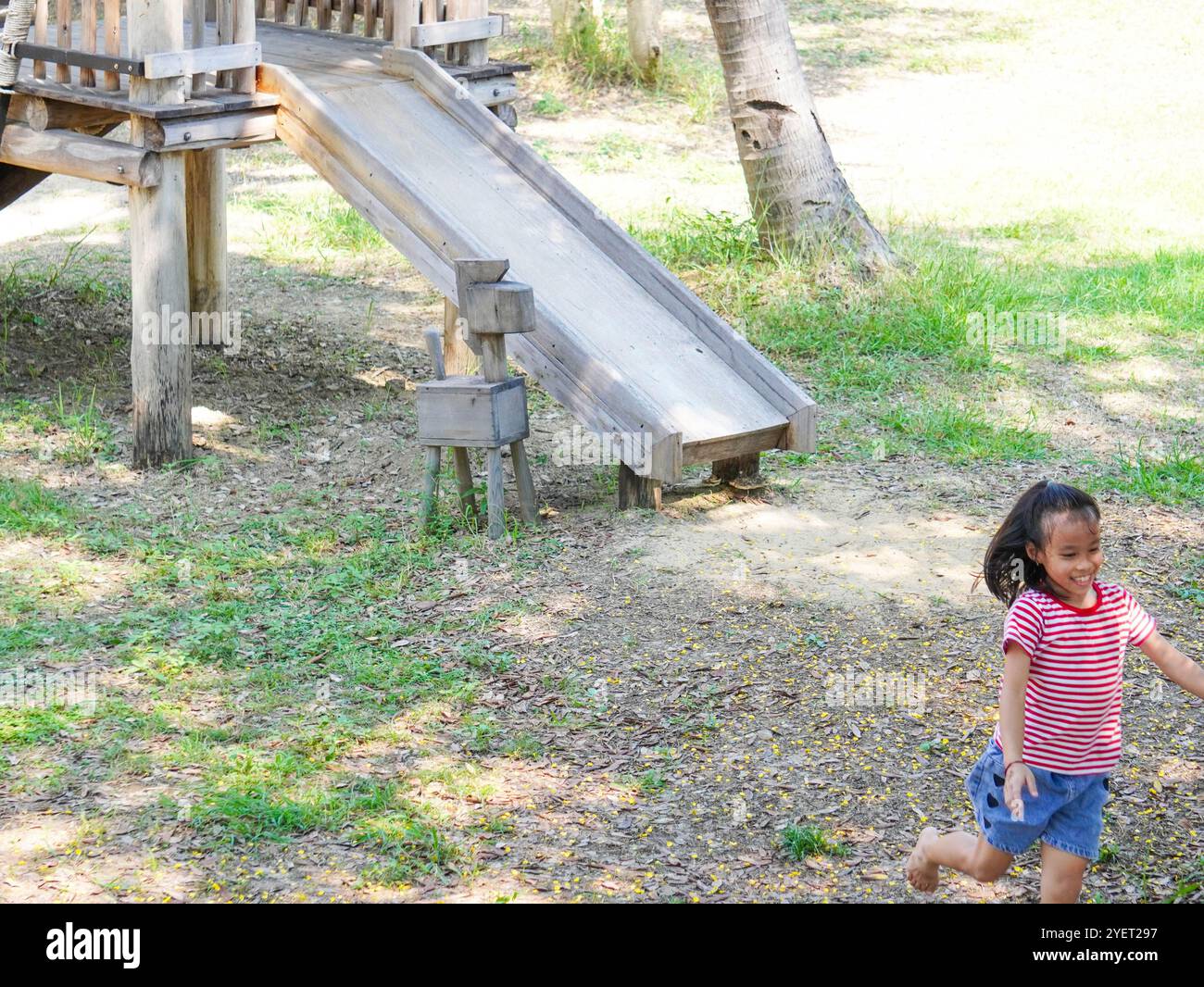 I bambini giocano all'aperto in un parco giochi in legno. Ragazza felice che gioca sullo scivolo nel parco giochi in estate. Foto Stock
