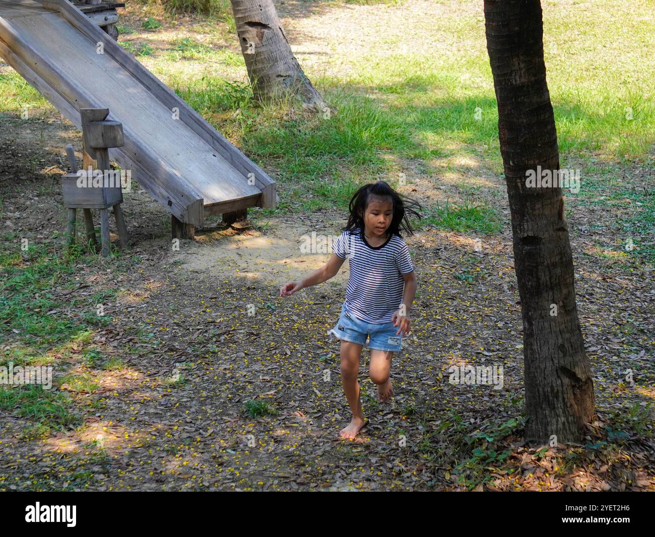 I bambini giocano all'aperto in un parco giochi in legno. Ragazza felice che gioca sullo scivolo nel parco giochi in estate. Foto Stock