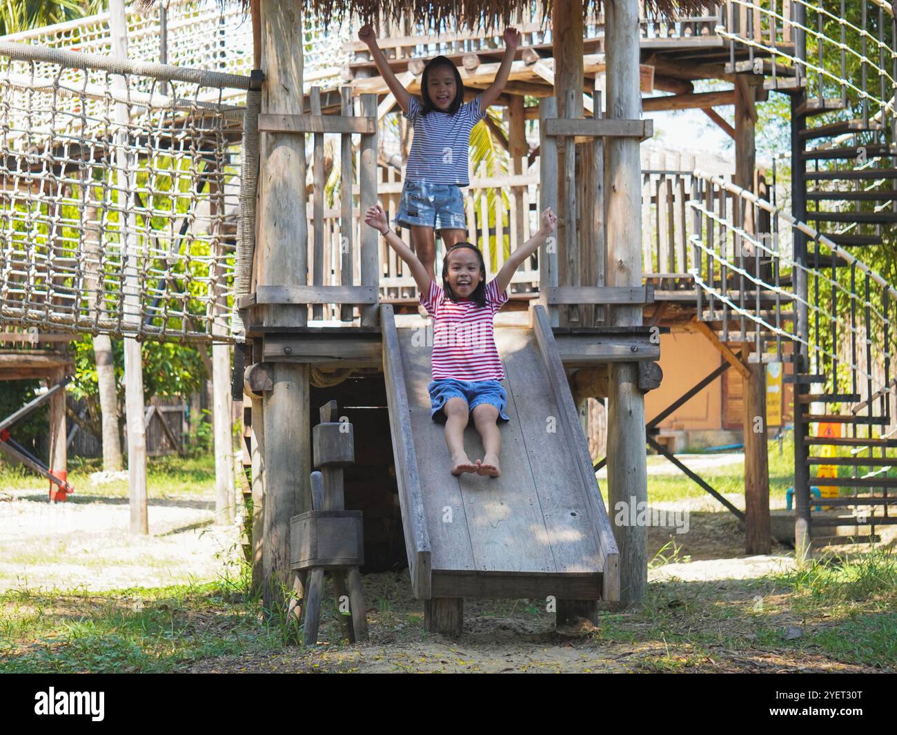 I bambini giocano all'aperto in un parco giochi in legno. Ragazza felice che gioca sullo scivolo nel parco giochi in estate. Foto Stock