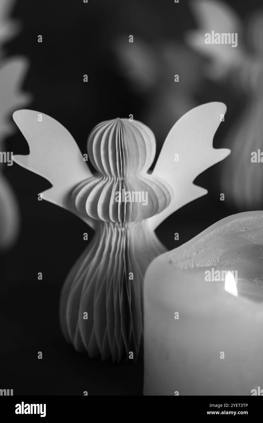 Angelo di carta fai da te su sfondo scuro. Simboli religiosi, decorazioni natalizie e Capodanno. Foto artistica in bianco e nero con basso profilo. Candele accese Foto Stock