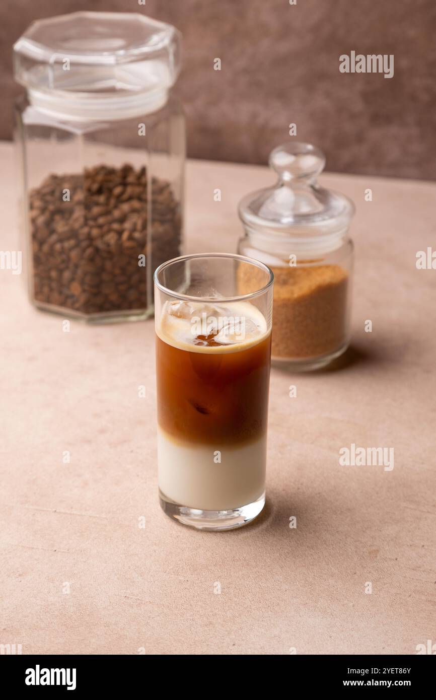 Caffè con latte di cocco e cubetti di ghiaccio in un bicchiere alto. Bevanda fredda analcolica tradizionale. Sullo sfondo, un vasetto di caffè e uno di zucchero. S Foto Stock