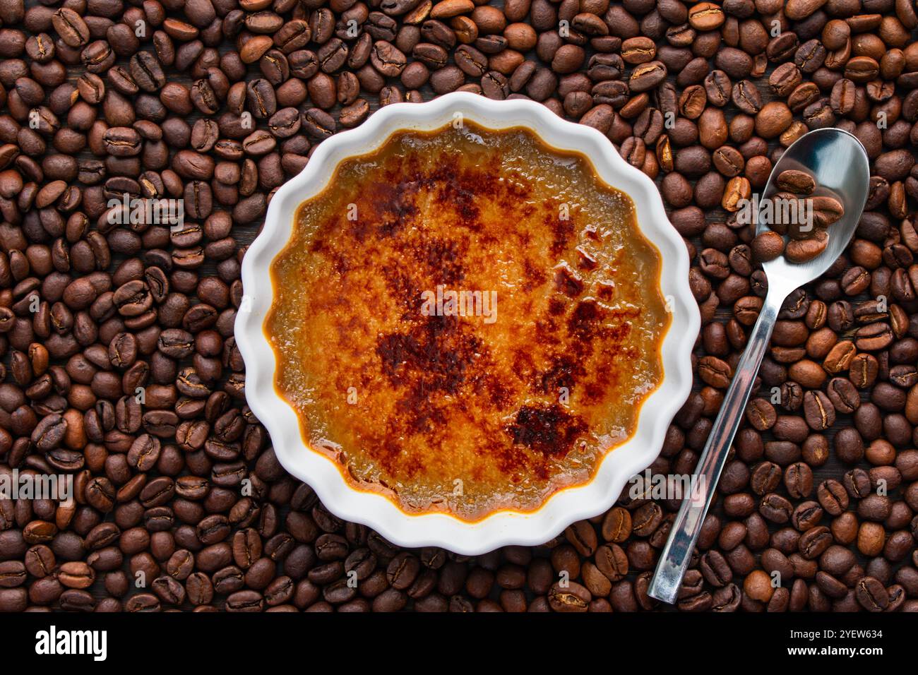 Coffee Creme Brulee e cucchiaio circondati da chicchi di caffè torrefatto: Ramekin poco profondo di creme brulee di caffè tormentato circondato da chicchi di caffè interi Foto Stock