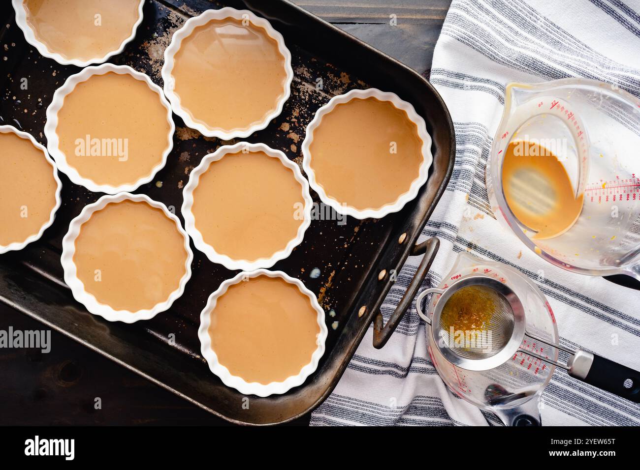 Creme Brulees di caffè non cotti in tovaglioli poco profondi: Otto camoule di ceramica bianca riempite con crema di caffè soffice in una grande teglia di tostatura Foto Stock