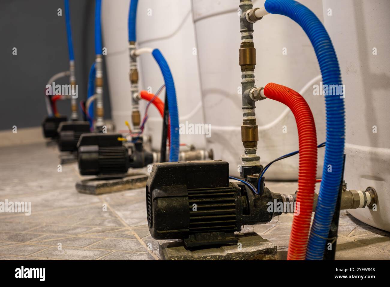 Primo piano di pompe dell'acqua industriali collegate con tubi flessibili blu e rossi in uno stabilimento. Apparecchiature essenziali per la gestione dei liquidi e il controllo del flusso. Foto Stock