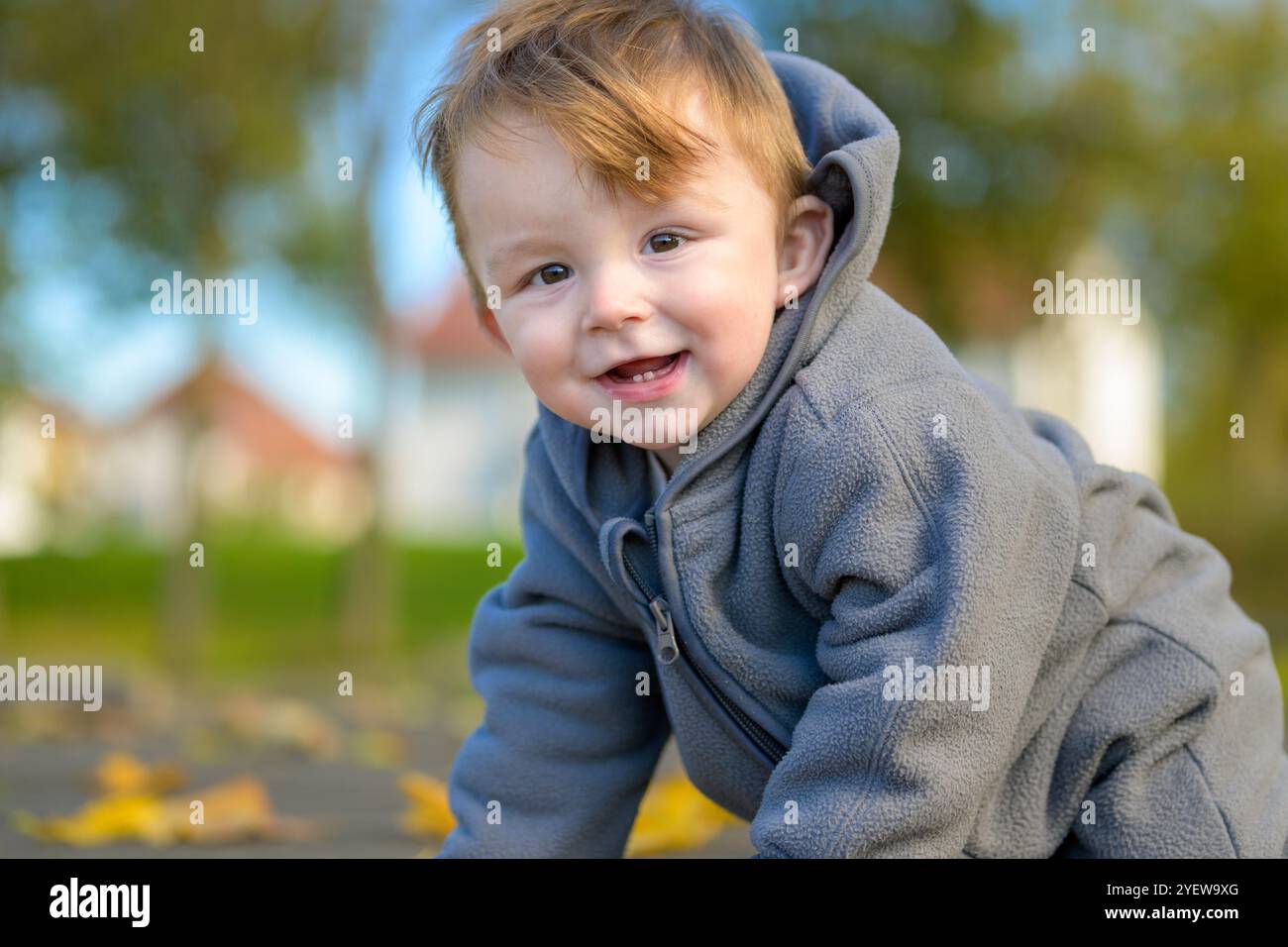 Un bambino allegro vestito con una calda giacca grigia sorride brillantemente mentre esplora l'aria aperta. Foto Stock
