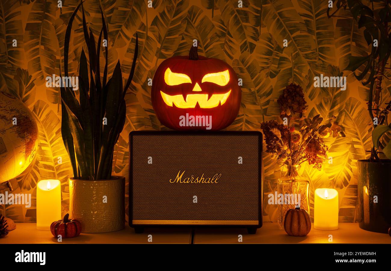 Altoparlante bluetooth Marshall decorato con tema Halloween. Zucca intagliata Jack-o'-lanterna posizionata sull'altoparlante circondata da candele. Foto Stock