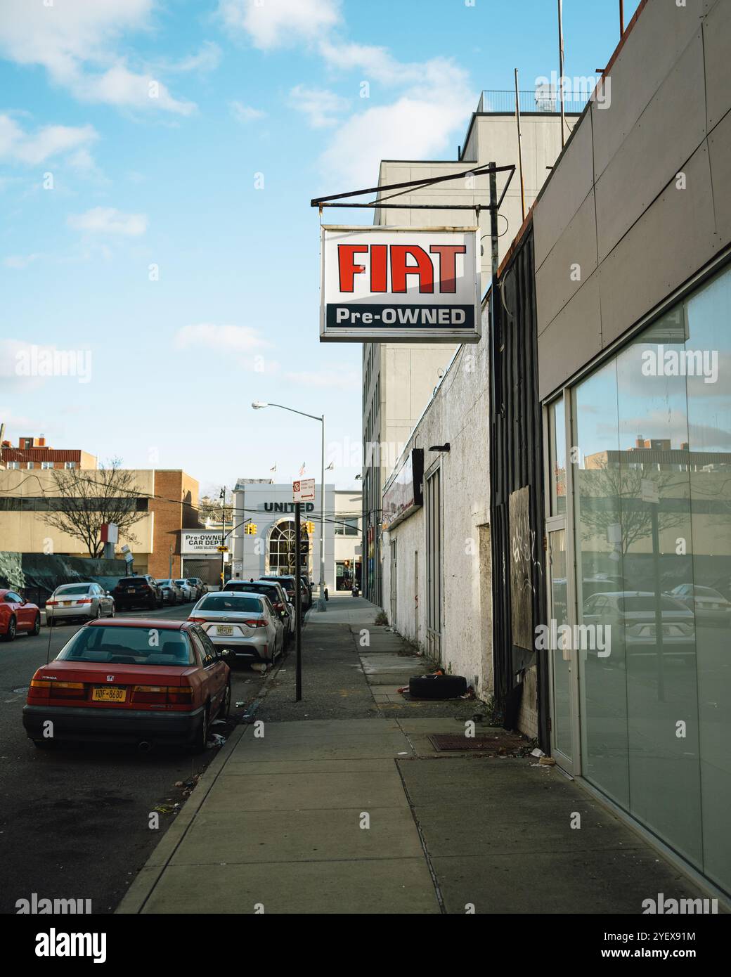 Una fila di auto parcheggiate fiancheggia una strada a Bay Ridge, Brooklyn, con un cartello Fiat usato appeso su un edificio. Foto Stock