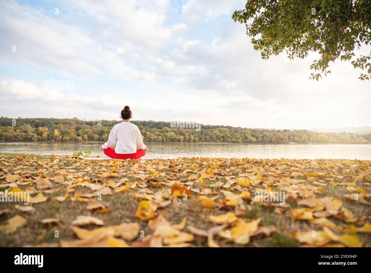 Yoga autunnale in natura. Donna che meditava vicino al fiume. Foto Stock