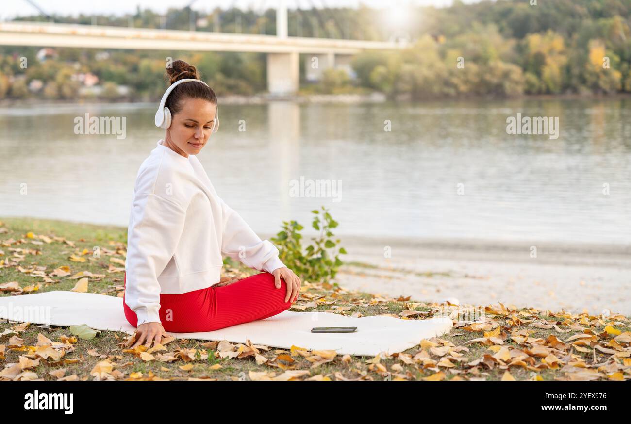 Benessere all'aperto. Donna che pratica yoga vicino al fiume in un giorno d'autunno. Foto Stock