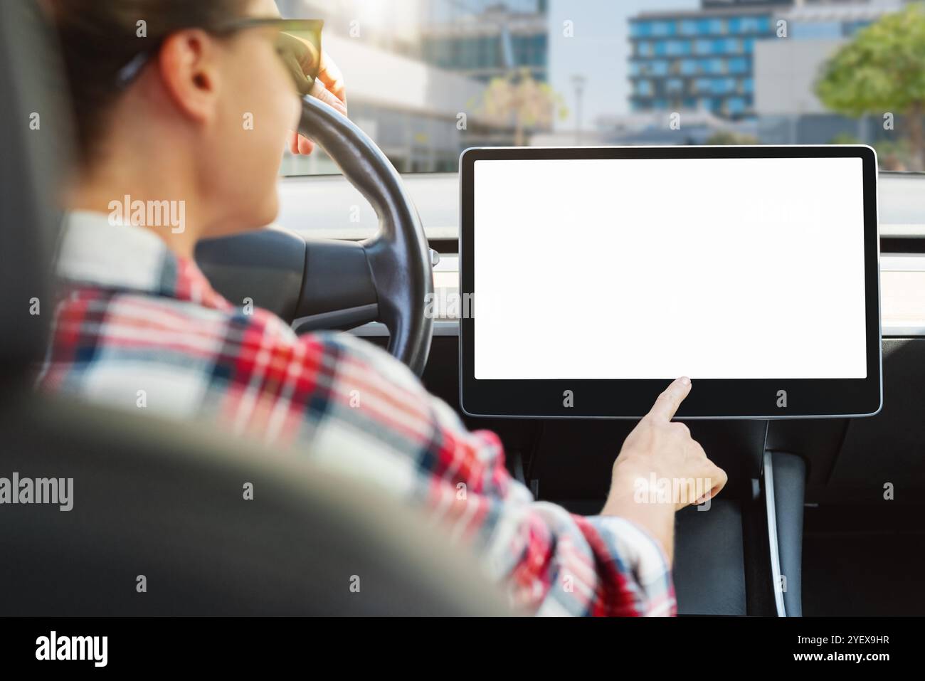 Il conducente donna interagisce con lo schermo di controllo digitale in un'auto moderna. Mockup dello schermo vuoto del sistema di informazione e intrattenimento. Foto Stock