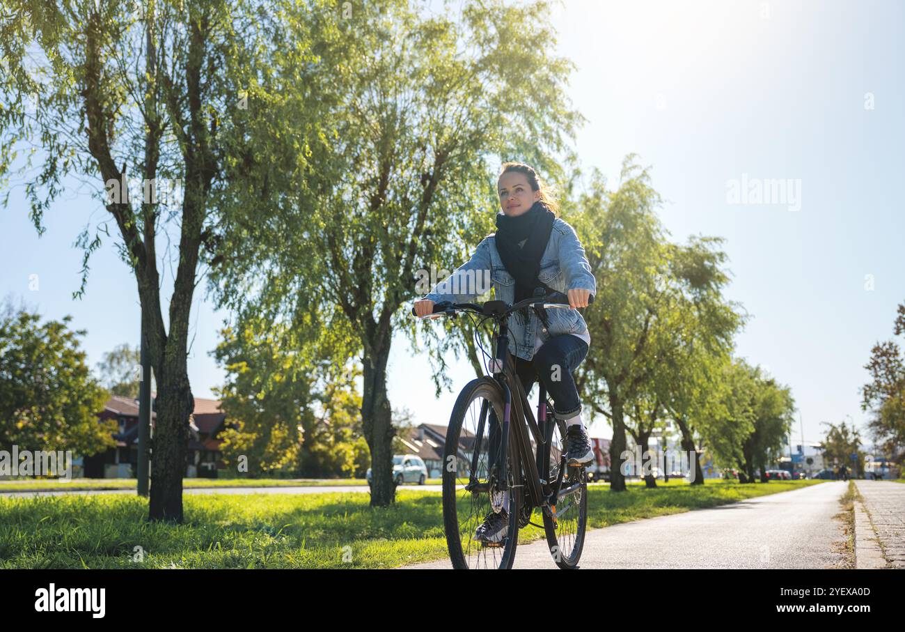 Donna in bicicletta fuori dal centro città, godendo di una fuga ringiovanente dalla vita urbana per migliorare la sua salute e il suo benessere. Foto Stock