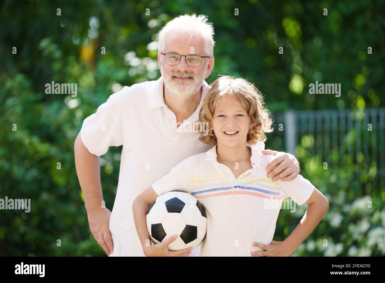 Nonno e bambini nel giardino soleggiato. Famiglia felice che gioca a football nel parco estivo. Nonno e bambini giocano a calcio. Amore di generazione. Senior attivo Foto Stock