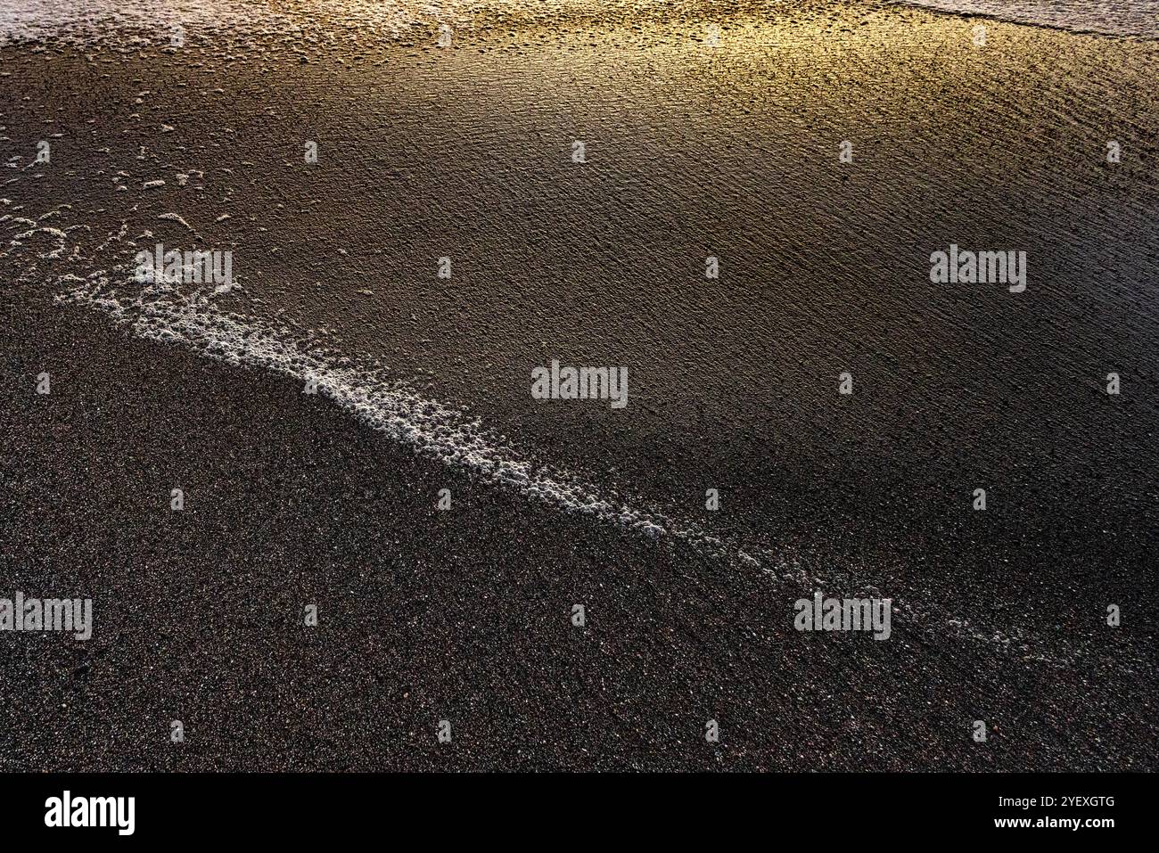 Onde su una spiaggia sabbiosa che formano splendidi motivi colorati nel bagliore del tramonto. Foto Stock