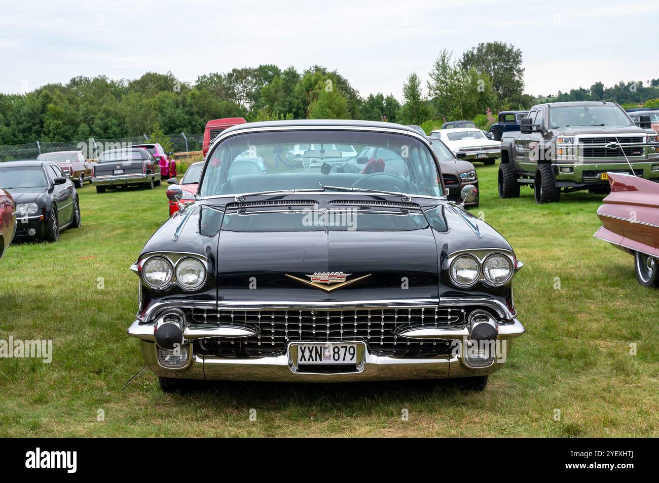 Una Cadillac nera ben mantenuta si erge orgogliosamente tra le numerose auto d'epoca, con gli appassionati che ammirano i veicoli d'epoca durante la mostra di auto all'aperto ev Foto Stock