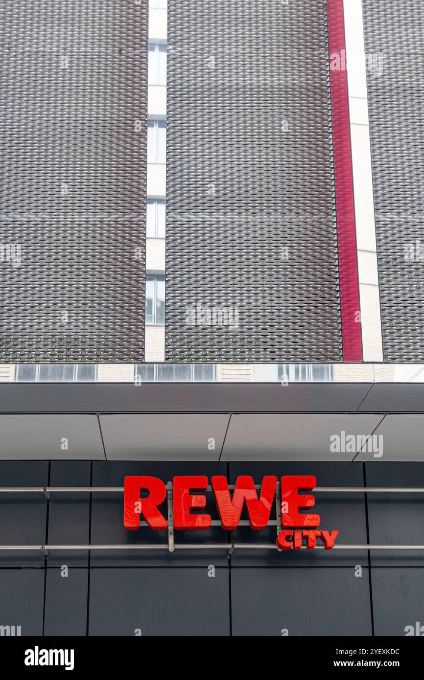 Francoforte, Germania - 26 ottobre 2024: Marchio REWE rosso con aggiunta "City" su una facciata grigia con elementi di design specchiati - spazio copia, negativo Foto Stock