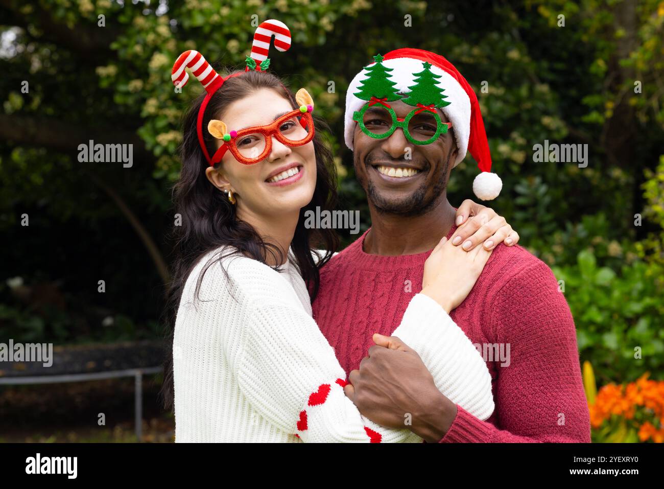 Coppia multirazziale sorridente che indossa occhiali e maglioni per festeggiare il Natale all'aperto Foto Stock