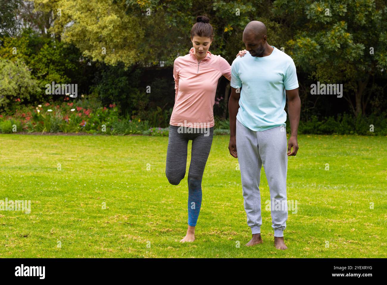 Allenati insieme sull'erba, coppia multirazziale che pratica fitness all'aperto e allenamento per l'equilibrio Foto Stock