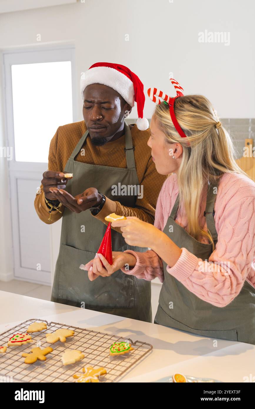 Adornare biscotti di Natale, coppia multirazziale che si diverte insieme in cucina, a casa Foto Stock