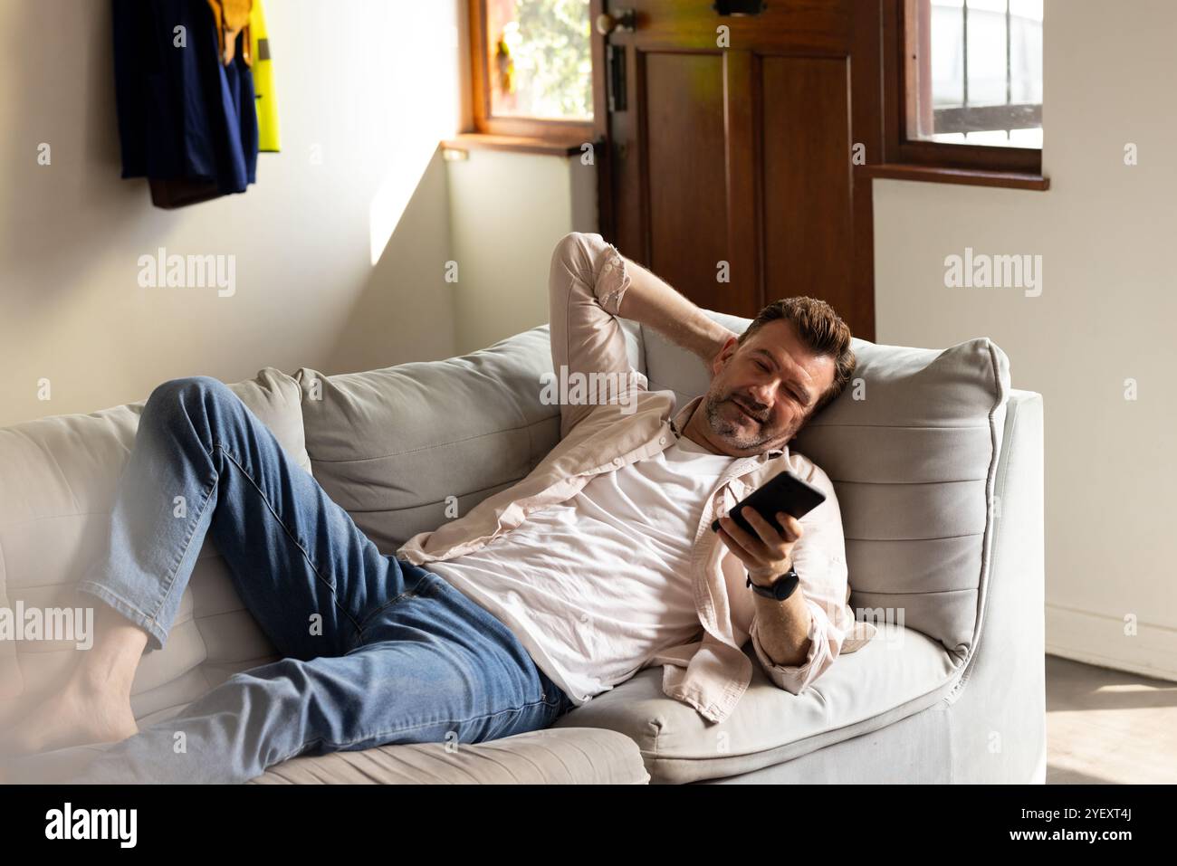 Rilassarsi sul divano, un anziano sorridente mentre utilizza lo smartphone a casa Foto Stock