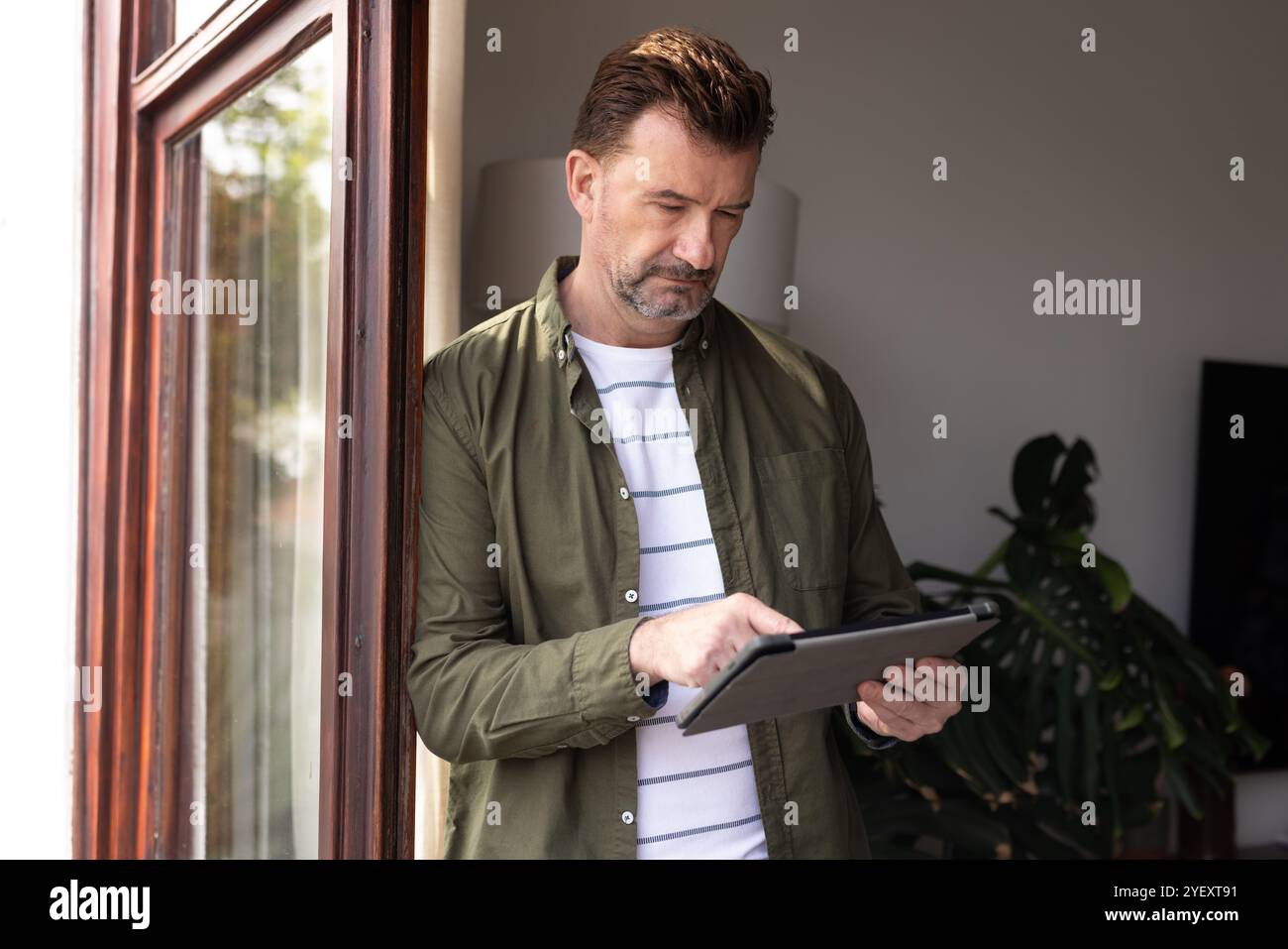 Uomo anziano maturo che utilizza un tablet a casa, concentrandosi sui contenuti digitali Foto Stock