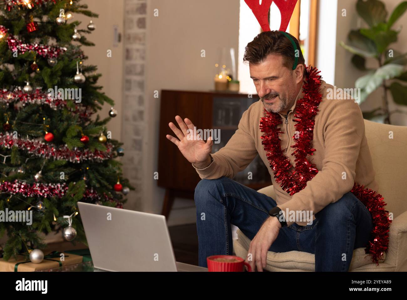 Uomo anziano che indossa corna di renne che chiacchiera video a casa durante il Natale Foto Stock