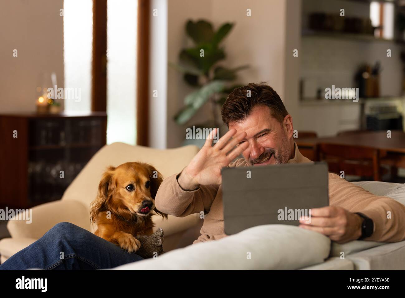 Un uomo anziano sorridente che chatta su un tablet con il cane a casa durante il Natale Foto Stock