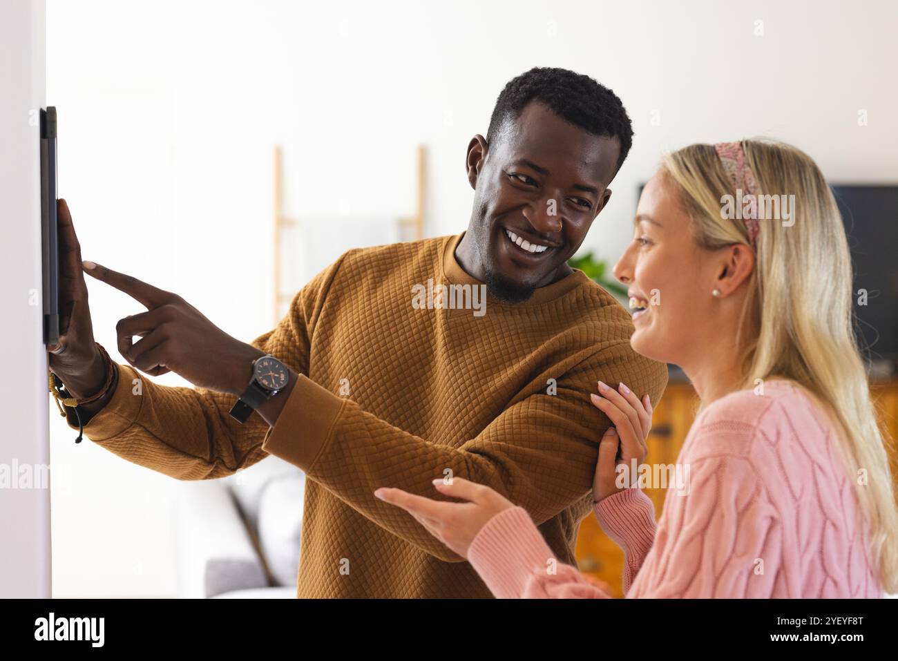 Coppia multirazziale sorridente che utilizza un dispositivo smart home a casa, per godersi la tecnologia insieme Foto Stock