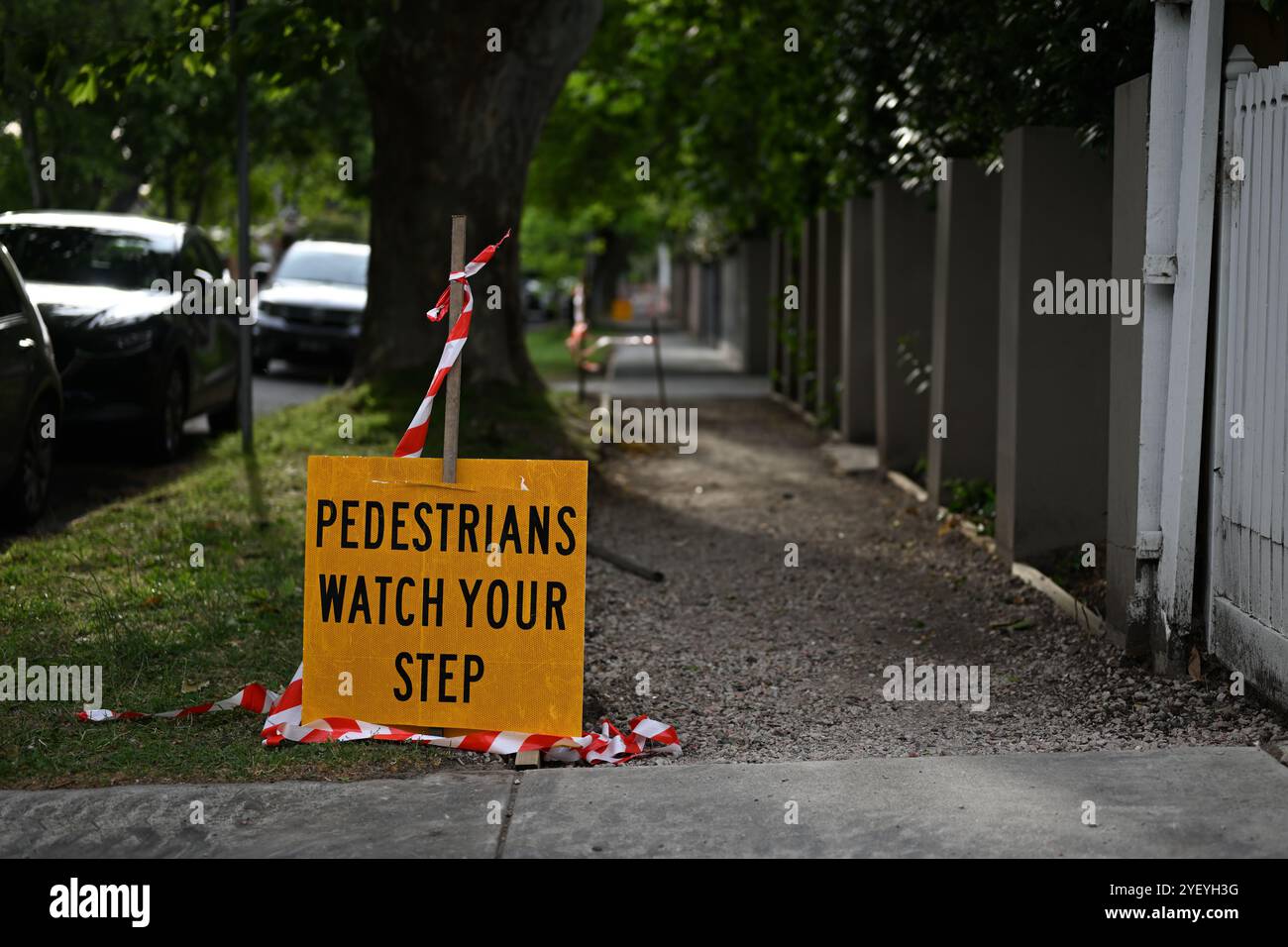I pedoni di colore giallo brillante osservano il tuo cartello con il testo nero, vicino a un tratto di sentiero non asfaltato, sotto alberi ombrosi in un sobborgo verde Foto Stock