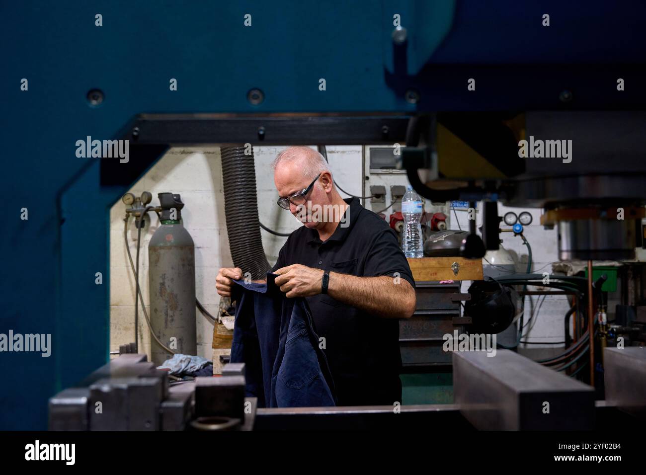 Lavoratore di metalli che ispeziona attentamente il tessuto vicino a macchinari industriali in un'officina metallurgica, dimostrando il controllo di qualità nella fabbricazione dei metalli Foto Stock