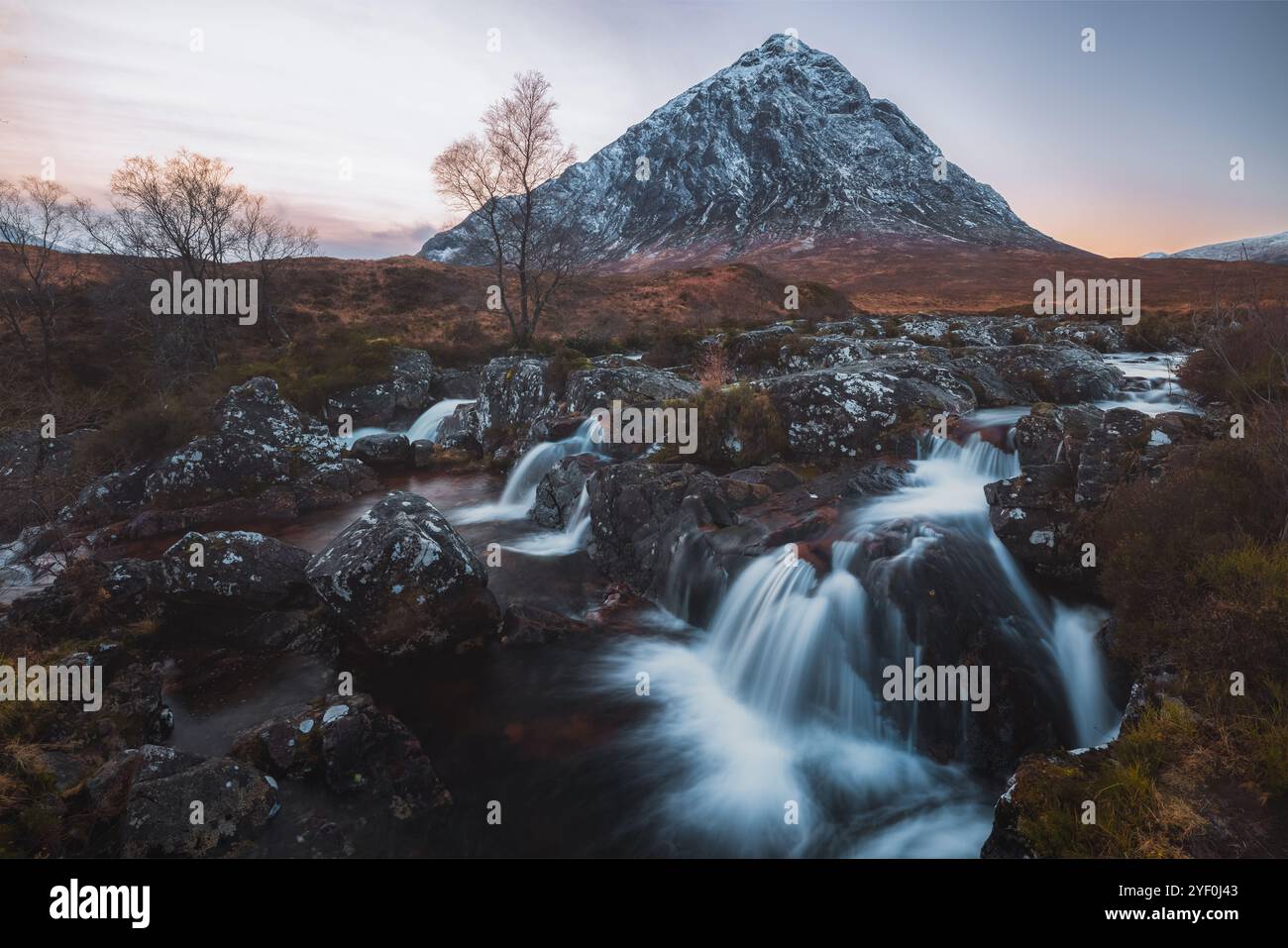 Una cascata scorre sotto la montagna innevata Buachaille Etive Mòr a Glencoe, in Scozia, mettendo in risalto la spettacolare bellezza dello Scottis Foto Stock