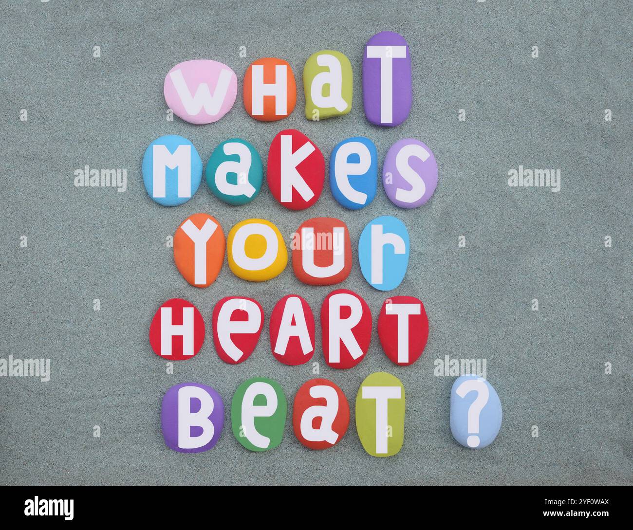 Ciò che fa battere il tuo cuore, domanda creativa e messaggio composto con lettere di pietra multicolori su sabbia verde Foto Stock