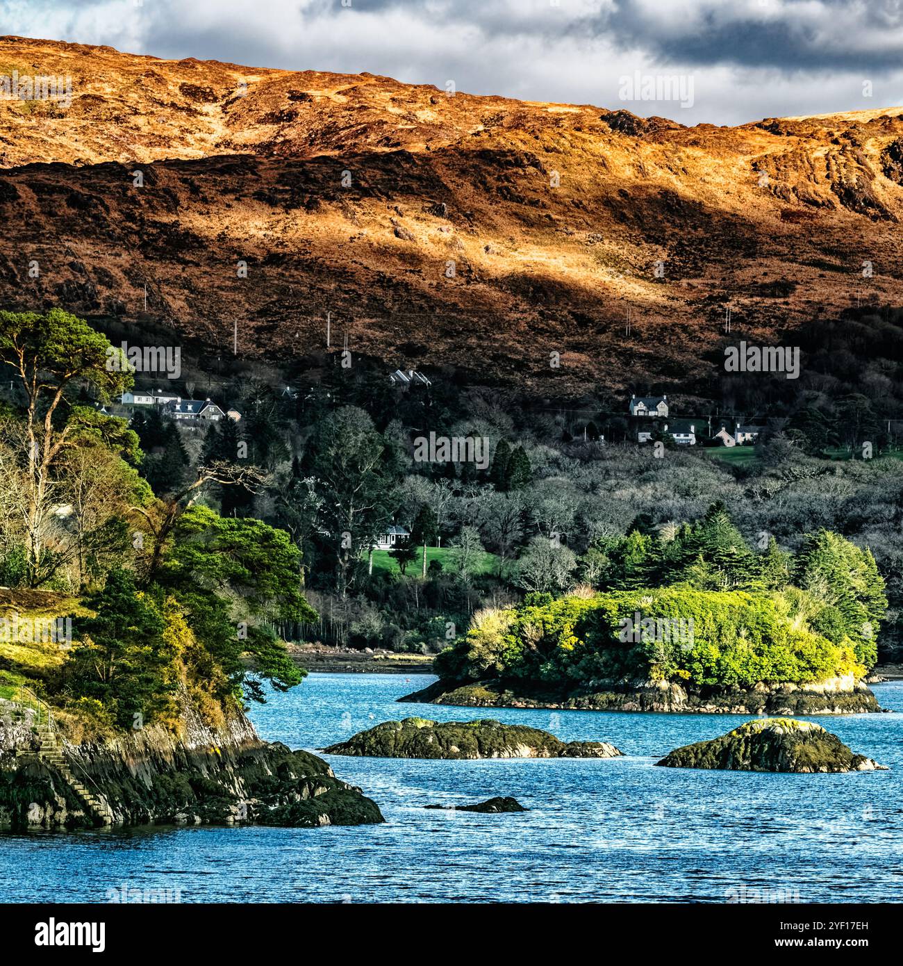 Una tranquilla baia rivela una vegetazione lussureggiante su piccole isole e suggestive colline illuminate dal sole che tramonta, creando un'atmosfera serena in Irlanda. Foto Stock