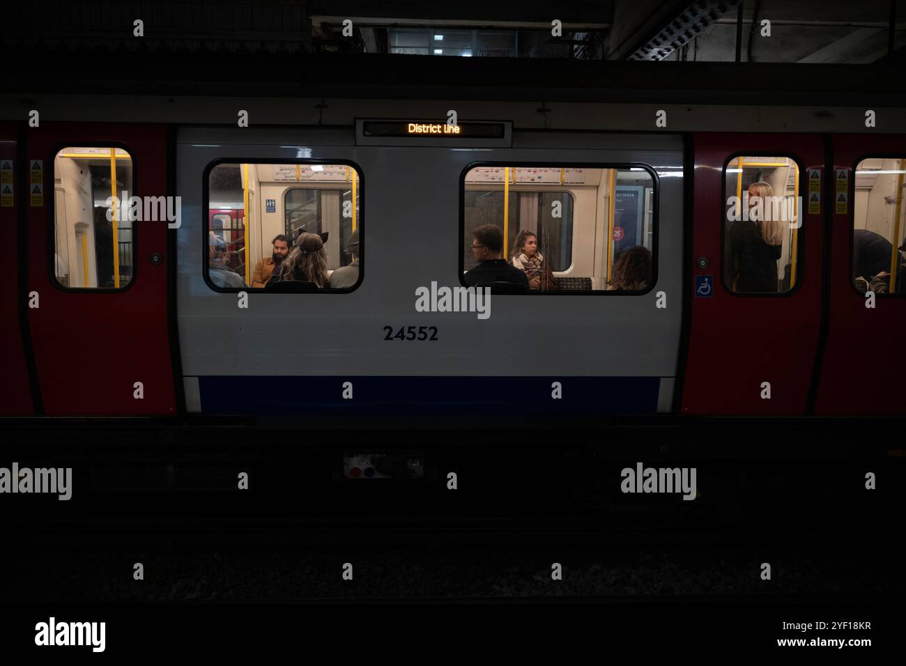 Viaggiatori notturni sulla District Line di Londra in direzione est con il sistema di trasporto della metropolitana di Londra, Inghilterra, Regno Unito Foto Stock
