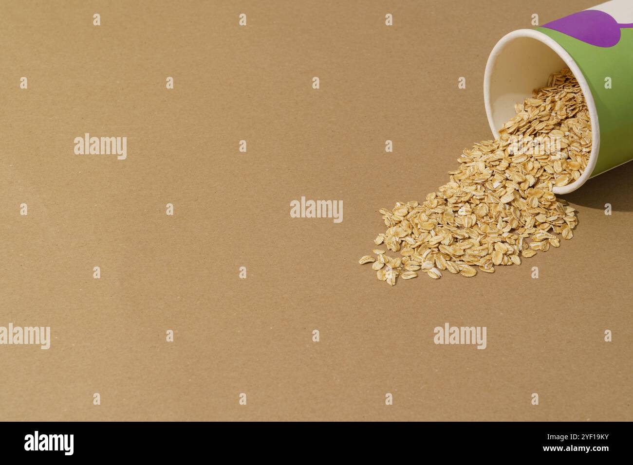 Un contenitore di carta che versa farina d'avena secca su uno sfondo marrone con spazio per le copie Foto Stock