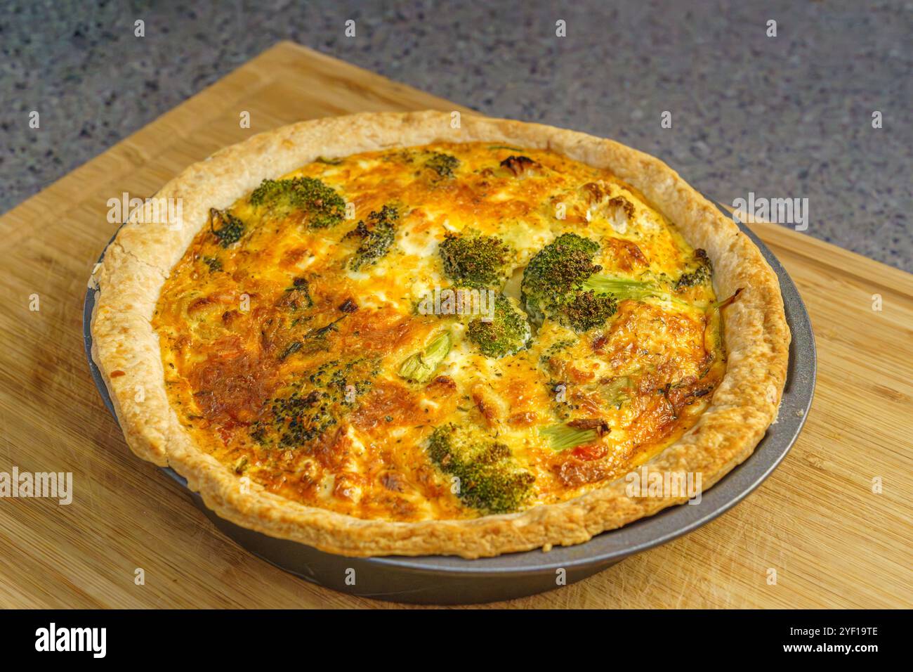 Un colpo ravvicinato di una quiche di crosta dorata piena di fiori di broccoli e un ripieno cremoso, cotto alla perfezione su un tagliere di legno. Foto Stock
