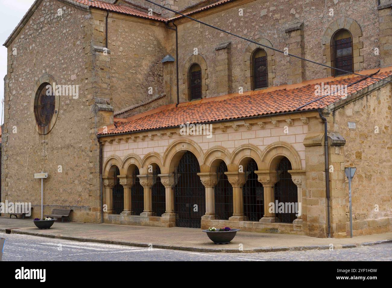 Un edificio storico in pietra caratterizzato da architettura romanica con finestre ad arco e tetto piastrellato. La struttura presenta una serie di colonne e archi a. Foto Stock